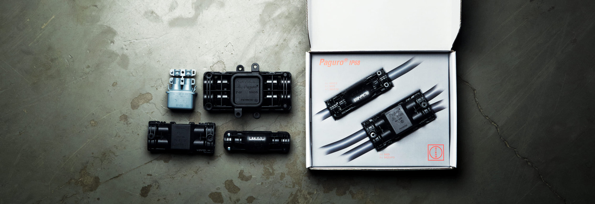 IP68-klassade kopplingsdosor och fördelningsdosor ur Paguro-serien från STEAB, uppställda på betonggolv med en öppen förpackning som visar inkopplade enheter.
