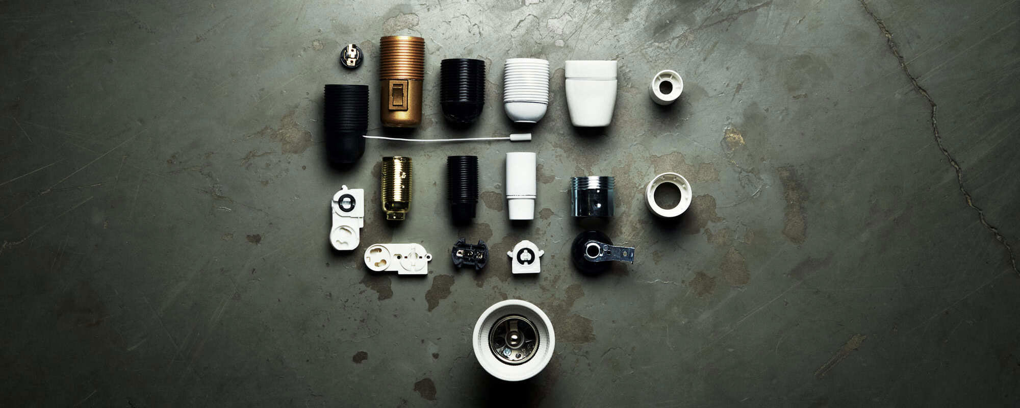 Ett urval av olika lamphållare och sockelkomponenter, inklusive modeller i plast, metall och porslin, arrangerade mot en mörk bakgrund.