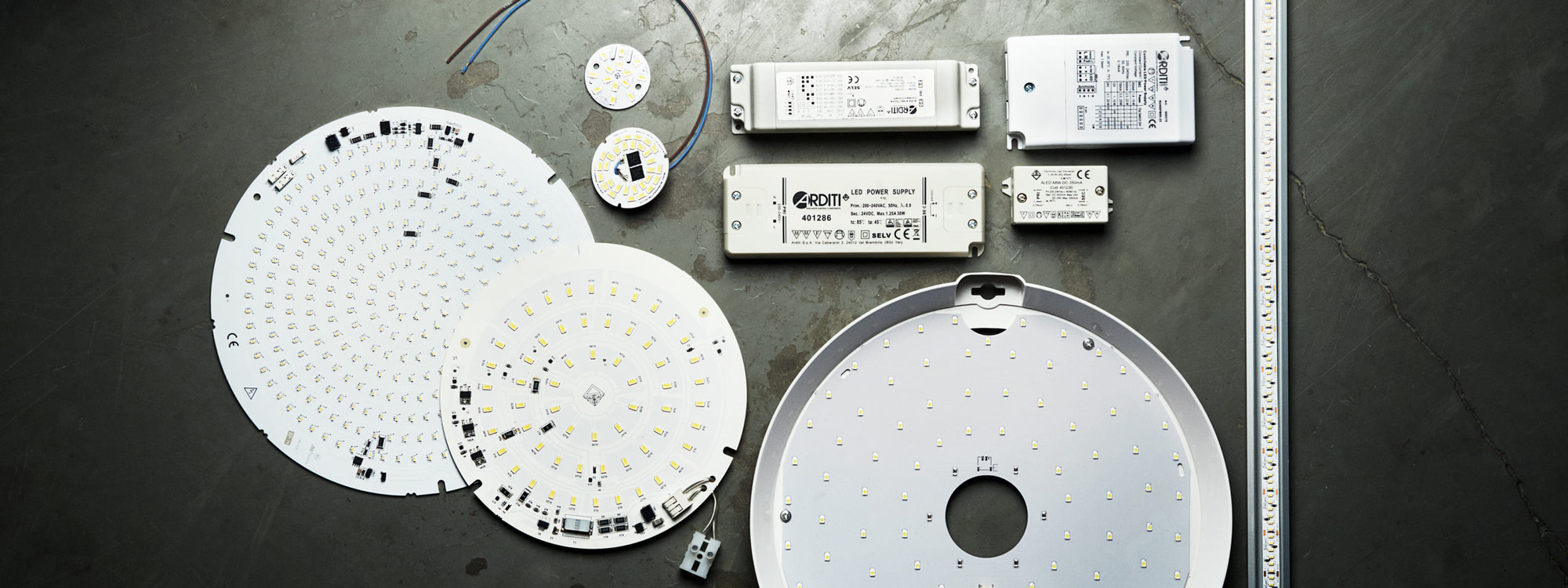 LED-moduler, drivdon och LED-strips uppställda på ett grått betonggolv – komponenter för professionell belysning i armaturbygge och installation.